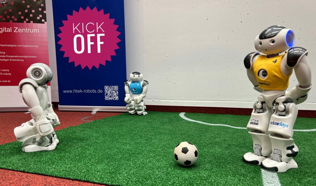 Roboter spielen Fußball auf einer grünen Matte.